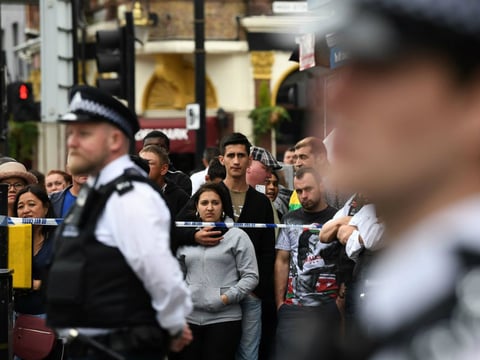 Londoners stand behind a cordon in the East Ham district on Sunday, following a police raid investigating Saturday's terror attacks in Central London.